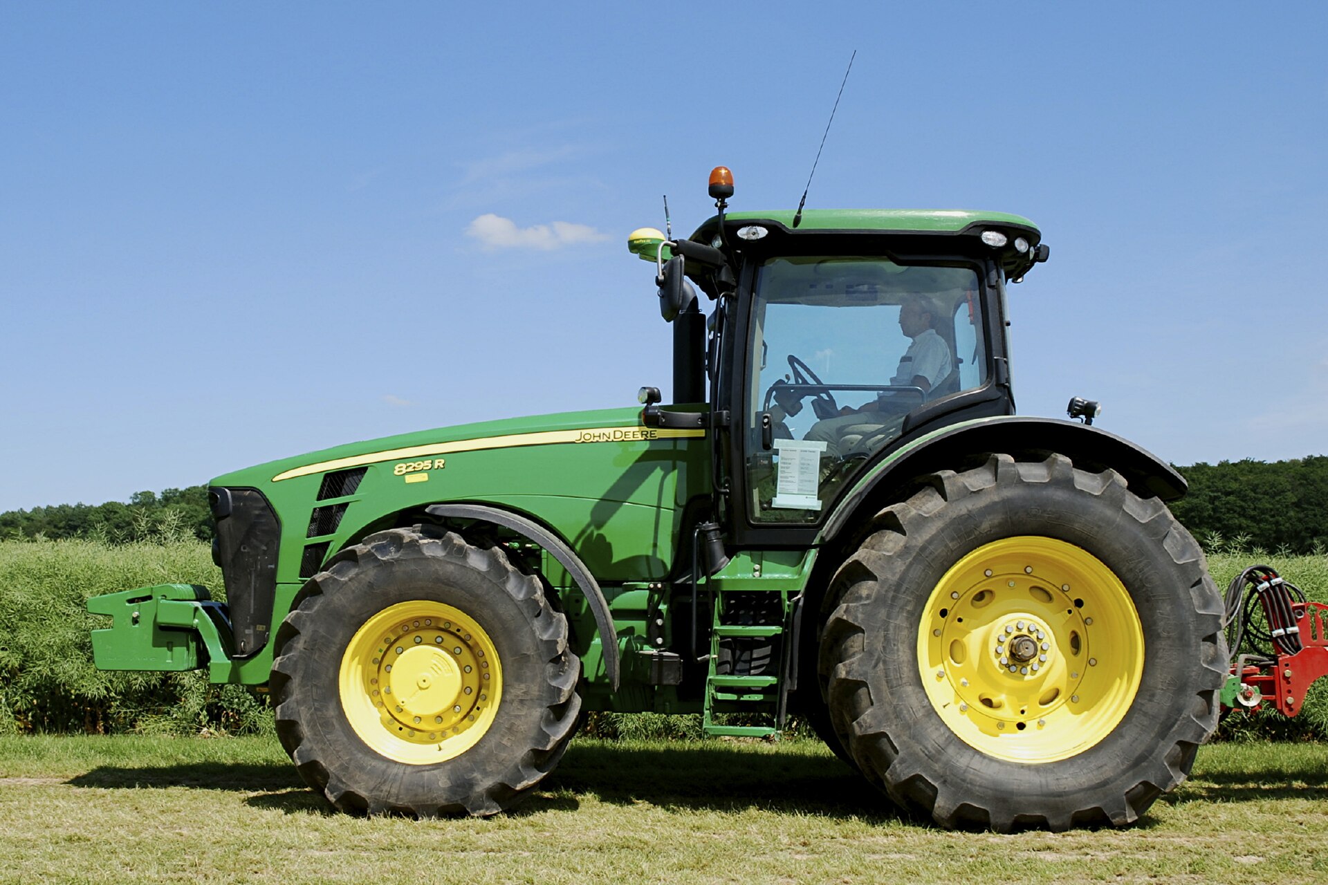 Trator agrícola de grande porte visto de perfil, com receptor GPS montado no teto da cabine para direção assistida por satélite