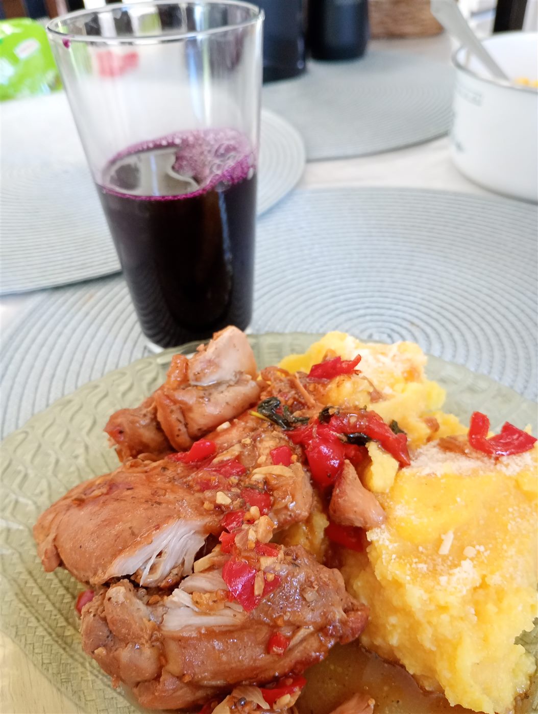 Prato com pedaços de galinha ao molho e polenta, ao lado de um copo de suco de uva, servidos à mesa